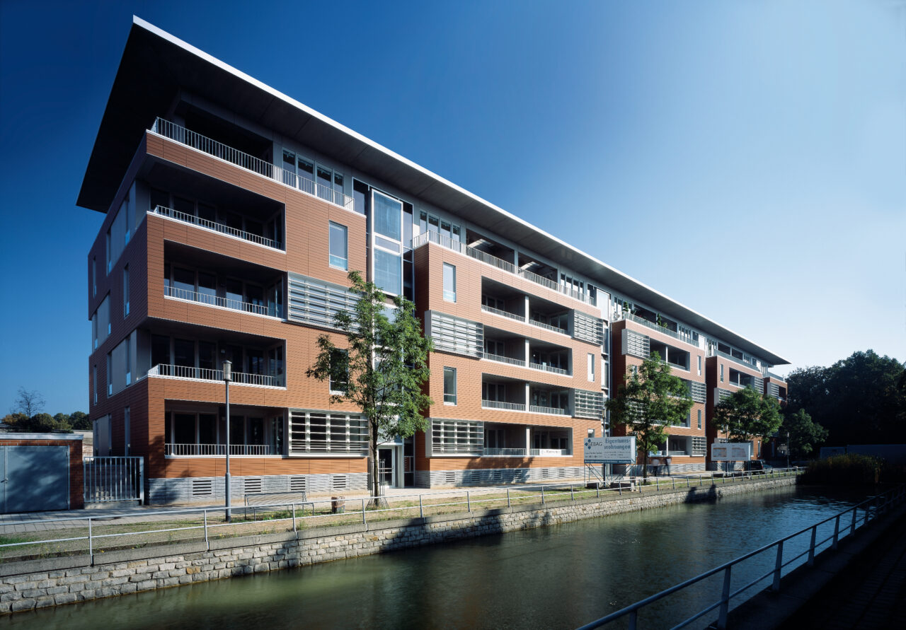 Wohnungsbauprojekt im Innenhafen Duisburg mit roten Keramikpaneelen, modernen Balkonen und großen Fenstern, entlang eines Kanals gelegen