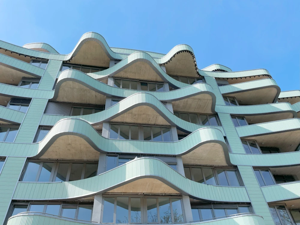 Tonality Keramikfassade am elliptischen Gebäude in Ljubljana, Frontansicht, die die wellenförmige Architektur und das moderne Design der Fassadenplatten zeigt.