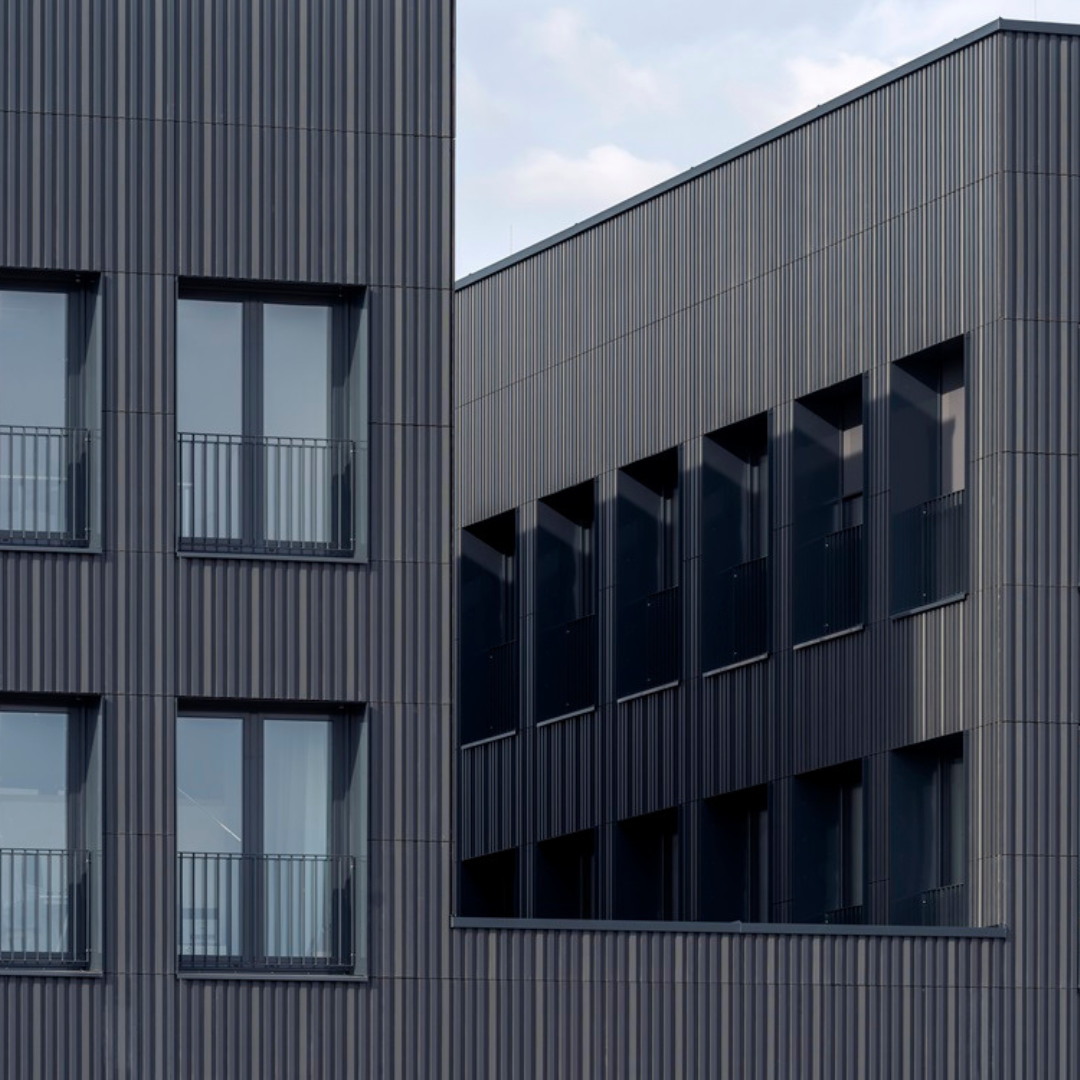 Modernes Gebäude mit dunkler Fassade und mehreren Fenstern, einige mit Balkongeländern.