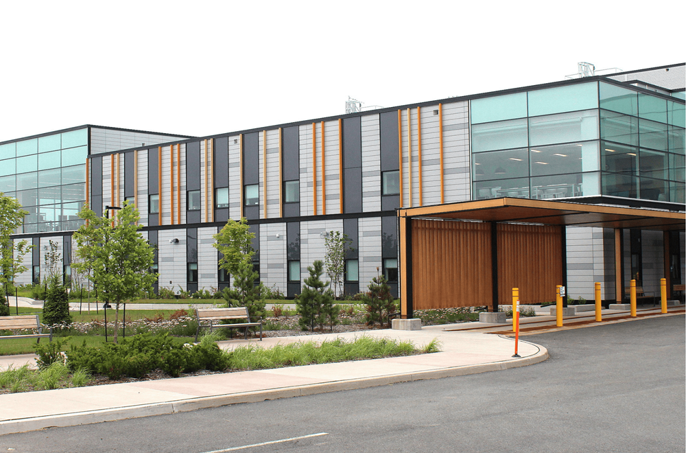 Modernes zweistöckiges medizinisches Zentrum mit Glasfassade und Holzverkleidung am Eingang, umgeben von Grünflächen.